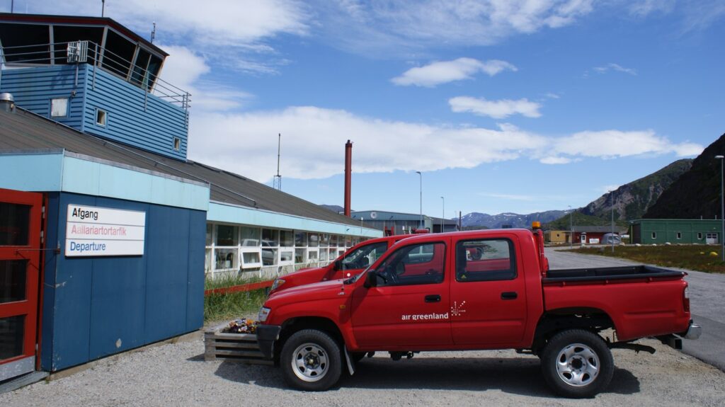 Blå terminalbygning med kontroltårn og rød pickup i Narsarsuaq