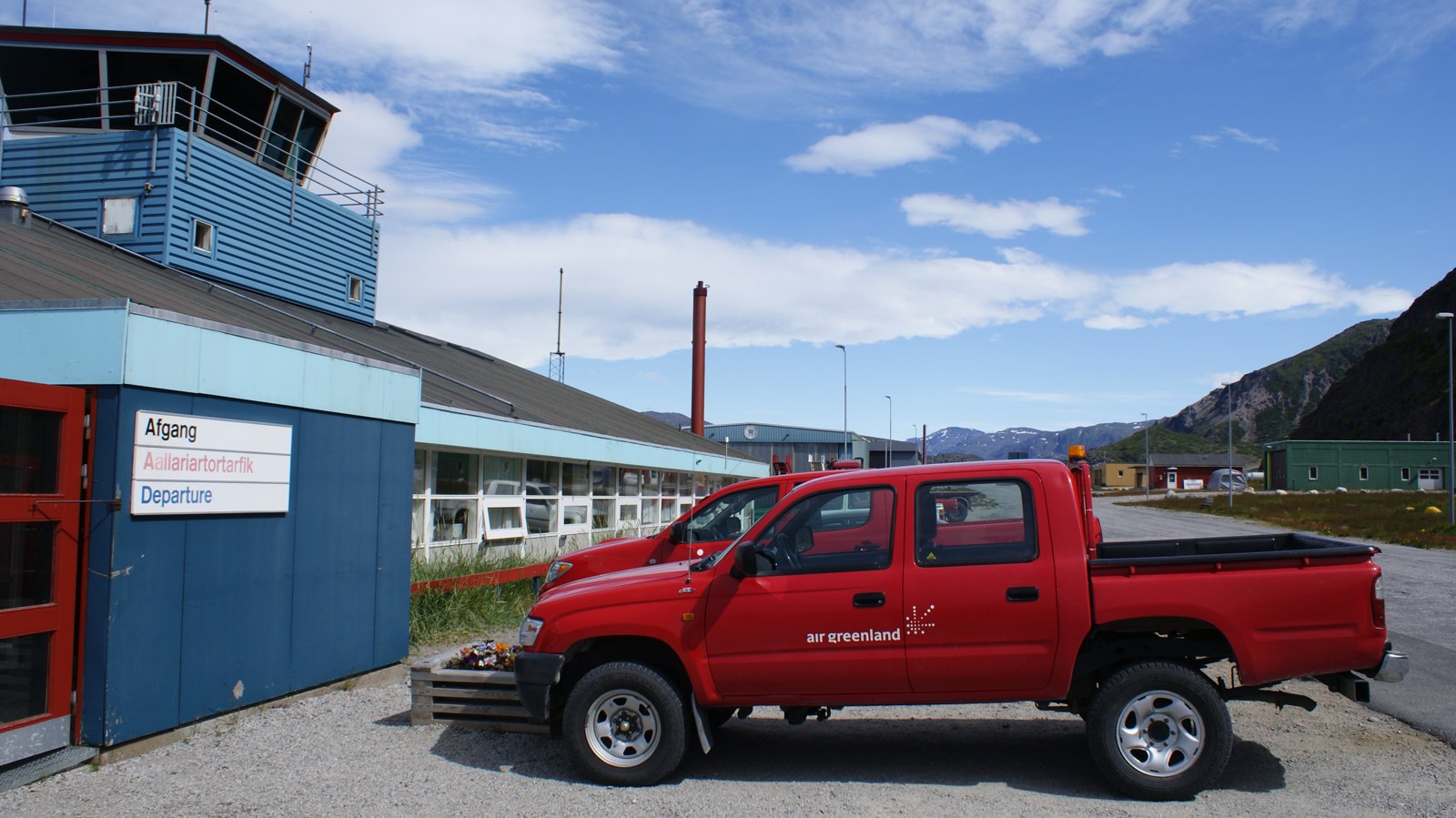 Blå terminalbygning med kontroltårn og rød pickup i Narsarsuaq